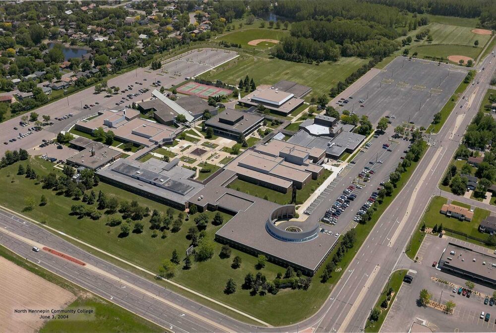 Aerial view of the low-rise North Hennepin Community College campus, showing large flat roofs, car parks and playing fields.
