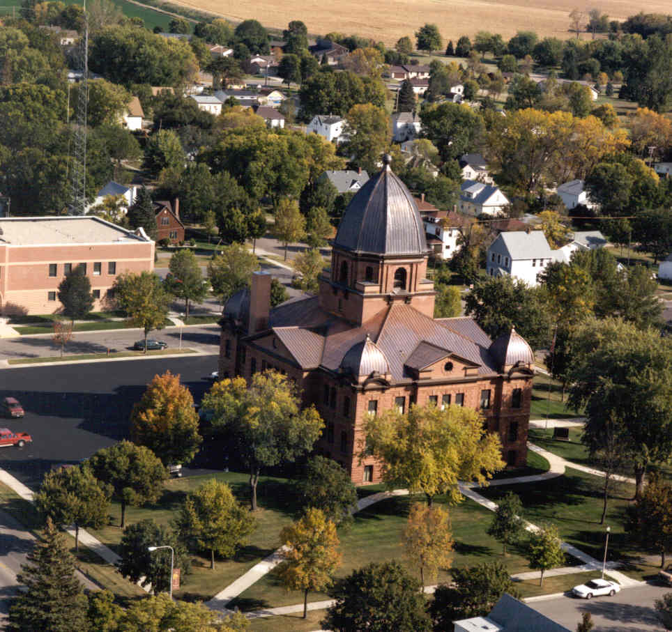 Aerial view of a red brick civic building with a domed tower and metal roofs, set among lawns and trees