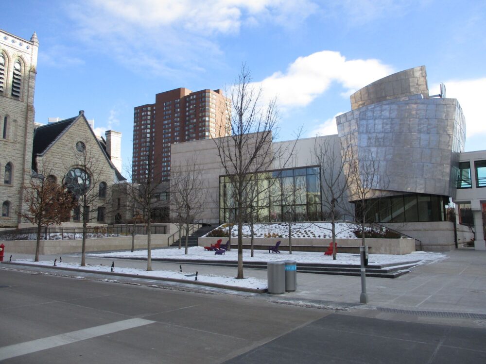 Westminster Church stone building beside a curved metal-clad addition and glazed wall, with a snow-dusted plaza.